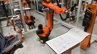 Industrieroboter in einer automatisierten Produktionszelle mit Bedienperson und Steuergerät.