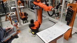 Industrieroboter in einer automatisierten Produktionszelle mit Bedienperson und Steuergerät.
