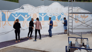 Mehrere Personen stehen vor einer Betonwand und besprühen diese mit Graffiti im Rahmen eines Workshops.