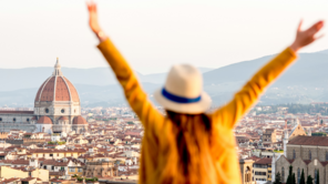 Young female tourist with raised hands looking on the old twon of Florence in Italy.