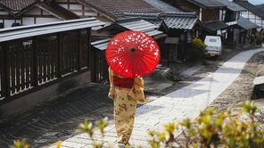 Eine Frau im traditionellen Kimono hält einen Schirm und läuft durch einen Ort in Japan.
