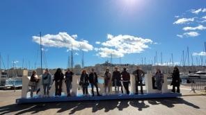 Gruppe von Studierenden am Hafen von Marseille, auf einem dort aufgestellten Schriftzug des Ortsnamens