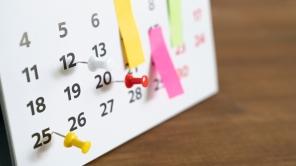 Bild von einem Kalender mit einigen Daten, die mit bunten Pins und Klebezetteln markiert sind.