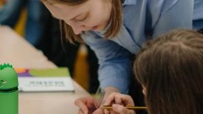 Klassenzimmer: studentische Lehrerin hilft einer Schülerin