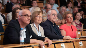 Die Uni-RektorÜ*innen sowie Wissenschaftsministerin Ina Brandes sitzen im Hörsaal und schauen zur Bühne.