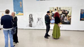 Menschen stehen vor Gemälden an einer weißen Wand und diskutieren darüber.