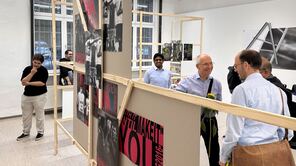 Menschen laufen durch die Rundgang-Kunstausstellung. Im Vordergrund ist ein Holz-Display zu sehen, an dem Fotografien hängen.
