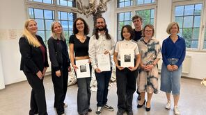Drei Kunstreisträger*innen halten ihre Urkunde hoch. Neben ihnen stehen Kanzlerin Iris Litty sowie Professor*innen aus dem Institut Kunst.