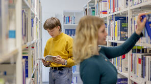Studierende sehen sich Bücher am Bücherregal an