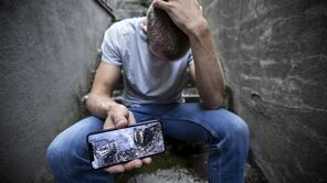 Mann hält Handy mit einem Foto von Zerstörung in die Kamera.