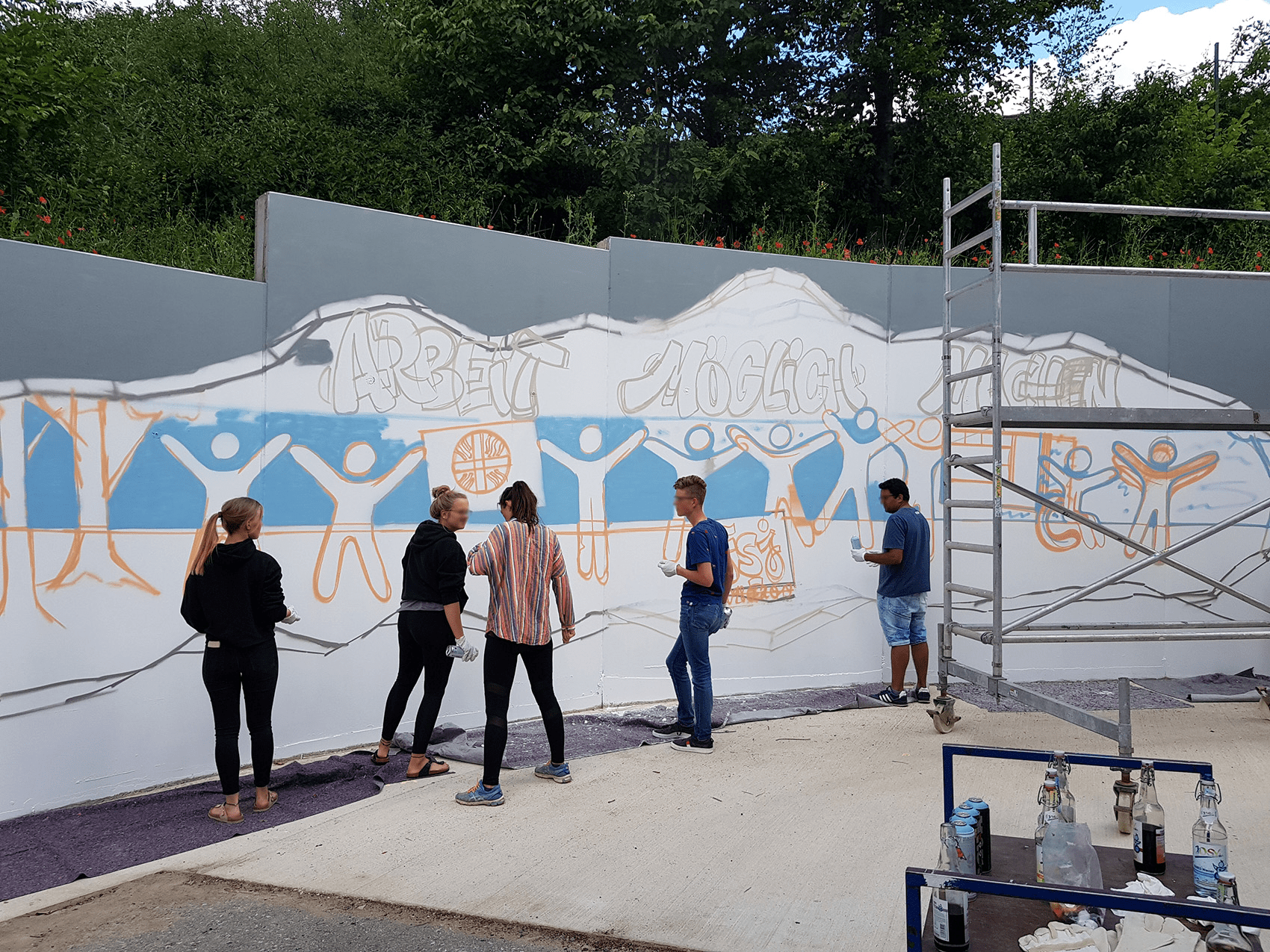 Mehrere Personen stehen vor einer Betonwand und besprühen diese mit Graffiti im Rahmen eines Workshops.