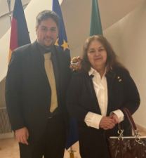 Dr. Hans Bouchard, Siggi und Prof. Dr. Sandra López Varela in der Residenz des deutschen Botschafters in Mexiko. Im Hintergrund eine Deutschland-, Europa-  und Mexikoflagge. Siggi hat ein Trikot der Pumas der UNAM an und sieht besonders elegant aus.