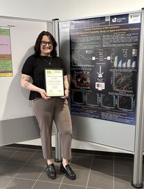 Désirée Anna-Maria Schütz mit Urkunde vor ihrem Poster.