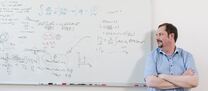Portrait Prof. Plätzer, vor einer beschriebenen Tafel mit Formeln