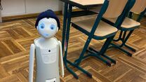 Kleiner Roboter mit Mütze steht neben einer Schulbank