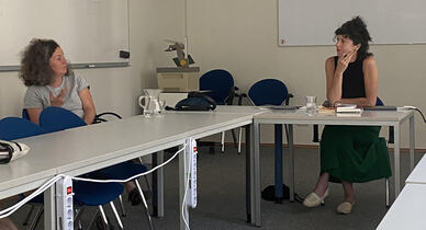 Zwei Frauen sitzen in einem Besprechungsraum an Tischen, links Regisseurin Carolin Schmitz, rechts Prof. Dr. Cornelia Wild,beide in Gesprächsposition.