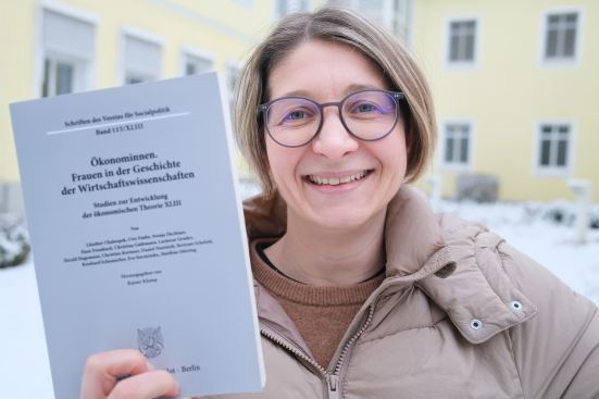 Junior-Professorin Dr. Svenja Flechtner vor der Charlotte-Leubuscher Haus am Campus US mit einem Buch in der Hand.