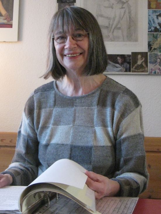 Doris Funk blättert in einem Buch und sieht freundlich in die Kamera