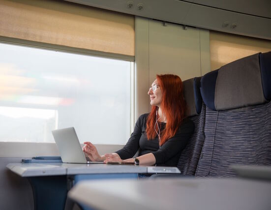 Weiblich gelesene Person, die im Zug an ihrem Laptop sitzt.