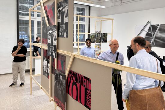 Menschen laufen durch die Rundgang-Kunstausstellung. Im Vordergrund ist ein Holz-Display zu sehen, an dem Fotografien hängen.