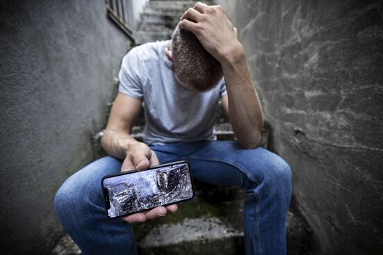 Mann hält Handy mit einem Foto von Zerstörung in die Kamera.