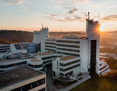Das Uni-Gebäude auf dem Campus Adolf-Reichwein-Straße bei Sonnenuntergang mit umliegender Landschaft und Hügeln im Hintergrund