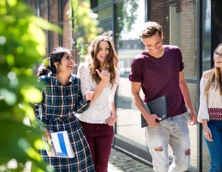 Eine Gruppe Studierender läuft fröhlich über einen Campus