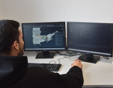 wissenschaftliche Hilfskraft simuliert am PC vor 2 Bildschirmen, links sieht man das Modell und rechts den Code