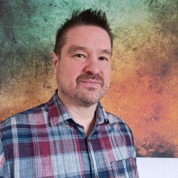 Profilfoto von Jörg Reifenberger, Gesicht und Oberkörper, im Hemd, vor buntem Hintergrund