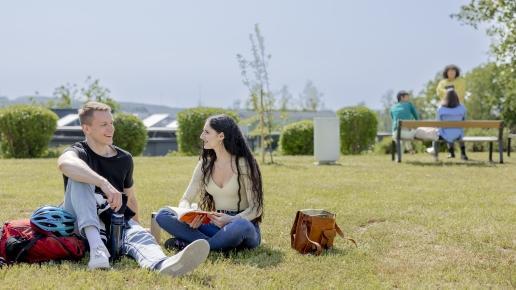 Studierende sitzen mit Rucksäcken und Büchern auf der LEOwiese.