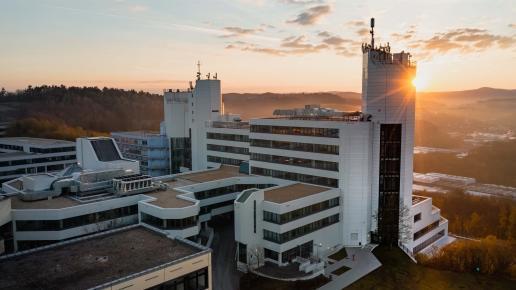 Das Uni-Gebäude auf dem Campus Adolf-Reichwein-Straße bei Sonnenuntergang mit umliegender Landschaft und Hügeln im Hintergrund