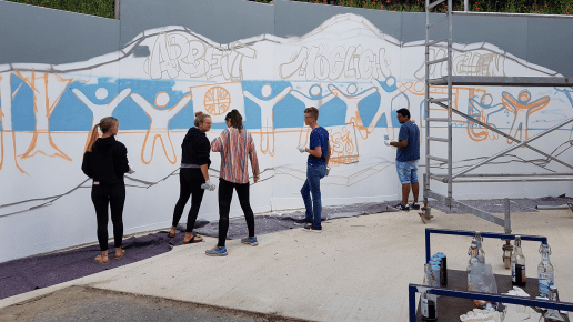 Mehrere Personen stehen vor einer Betonwand und besprühen diese mit Graffiti im Rahmen eines Workshops.