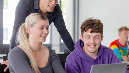 Studierende im Seminarraum schauen gemeinsam auf einen aufgeklappten Laptop