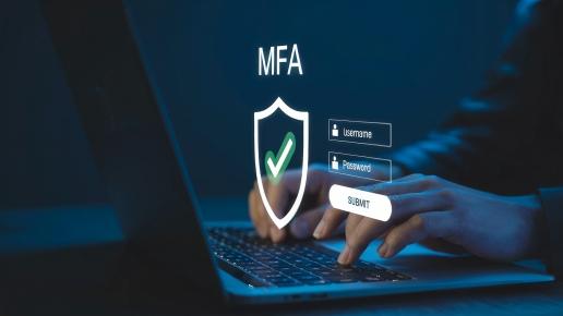 Hände vor einem Laptop mit einer Login-Maske. Neben der Tastatur schwebt ein Verteidigungsschild mit der Überschrift "MFA" und einem grünen Haken.