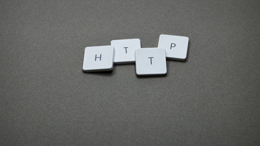 Das Bild zeigt vier weiße Tastenkappen mit den Buchstaben „H“, „T“, „T“ und „P“, die lose auf einer grauen Oberfläche liegen. Die Anordnung stellt die Abkürzung „HTTP“ dar, die für „Hypertext Transfer Protocol“ steht – das Standardprotokoll für die Übertragung von Daten im World Wide Web.