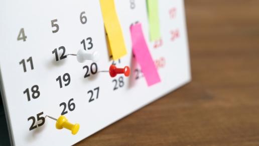 Bild von einem Kalender mit einigen Daten, die mit bunten Pins und Klebezetteln markiert sind.