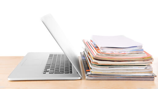Aufgeklappter Laptop und ein Stapel Zeitschriften