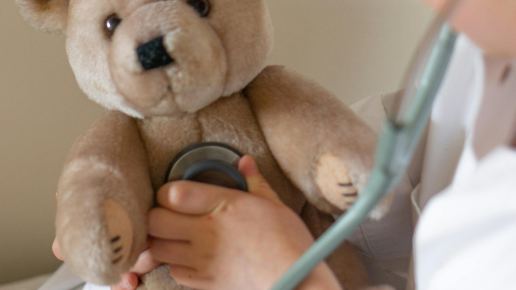 Kind hört einen Teddybär mit einem Stethoskop ab.