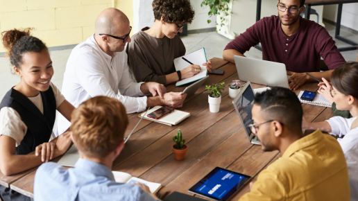 Menschen sitzen in mit Laptops und Notizbüchern um einen Holztisch.