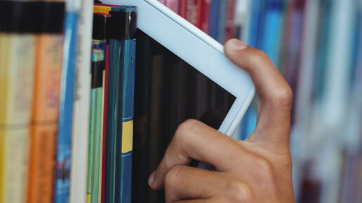 Eine Hand entnimmt ein Smartphone aus einem langen Bücherregal