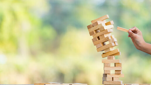 Ein Jenga-Turm stürzt und eine Hand hält einen Block
