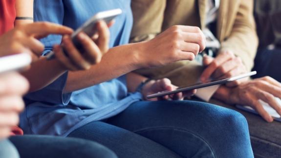 Sitzende Menschen bedienen verschiedene Geräte wie Laptops und Tablets