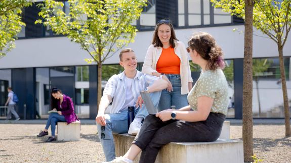 Drei Studierende auf Sitzblöcken auf dem Campusgelände