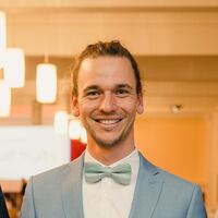 Philipp Spelten, hellblauer Anzug, hellgrüne Fliege, lange Haare im Zopf, breites Lächeln